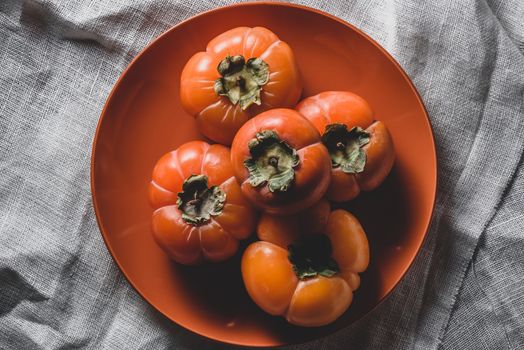 Few fresh persimmons on orange plate. View from above