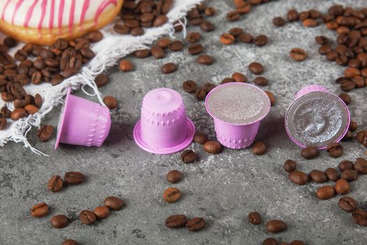 Espresso pink plastic capsules with foil and coffee beans and sweet donuts on gray concrete background