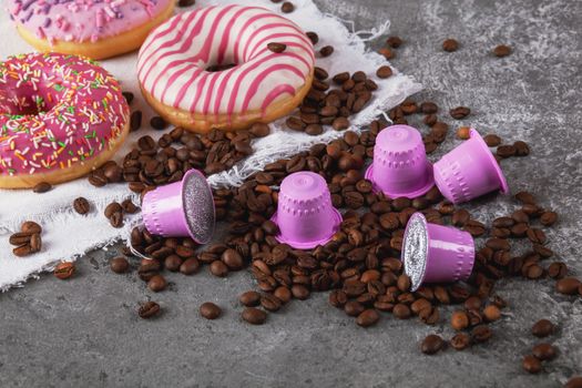 Espresso pink plastic capsules with foil and coffee beans and sweet donuts on gray concrete background