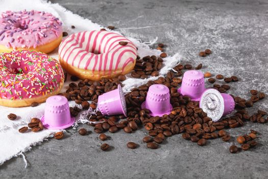 Espresso pink plastic capsules with foil and coffee beans and sweet donuts on gray concrete background