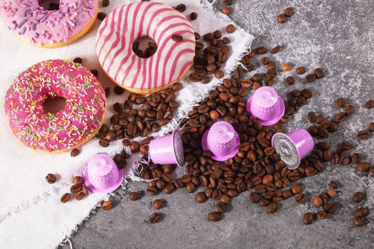 Espresso pink plastic capsules with foil and coffee beans and sweet donuts on gray concrete background
