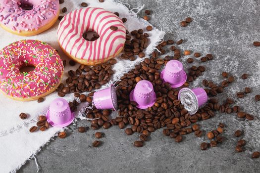 Espresso pink plastic capsules with foil and coffee beans and sweet donuts on gray concrete background
