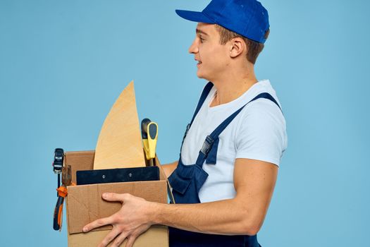 working man in uniform box with tools loader delivery blue background. High quality photo