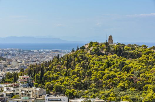 View of the monument to Filopappos on the hill of the same name the city of athens and in the background you get to appreciate the port of the piraeus and the sea