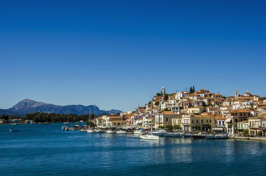 Port of the island of poros in the Saronic sea with its moorings of yachts the harbor district and at the top of the hill its famous clock tower