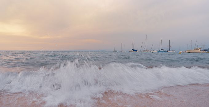 At sunset the waves break on the beach in front of boats, Italian landscape