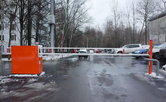 Closed barrier at the entrance to the courtyard of a multi-storey residential building in winter.