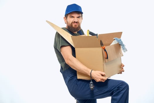 Worker man in uniform with a box in his hands tools delivery service light background. High quality photo