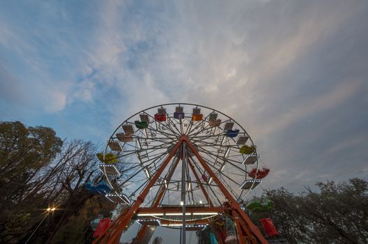 Ferris wheel bottom view in the early evening under blue sky at sunset, street photography landscape