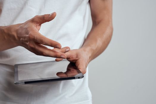 Tablet with a touch screen on a light background male hands white t-shirt cropped view. High quality photo