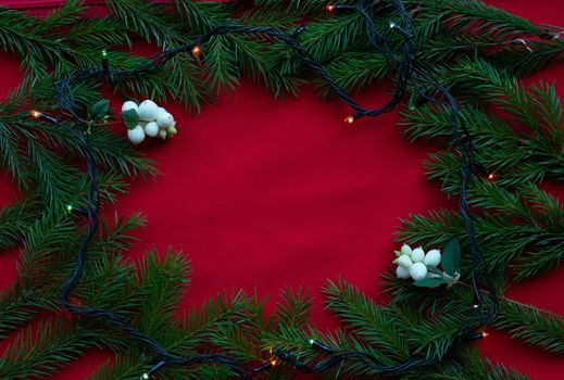 Frame of green fir branches and white dogwood berries on a red background. The concept of Christmas and the new year. Space for your text.