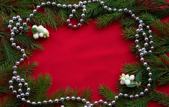 Frame of green fir branches and white dogwood berries with silver beads on a red background. The concept of Christmas and New year. Space for your text.