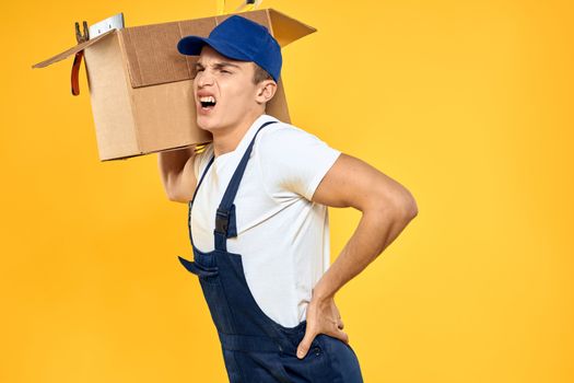 Working man in uniform with box hand delivery loading service yellow background. High quality photo