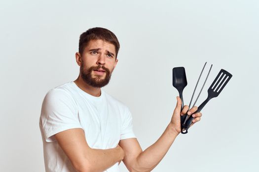 A man with kitchen appliances in the hands of their white T-shirt on a light background cropped view. High quality photo