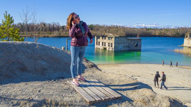 Hiker on mountain top. Woman is standing with an Abandoned Quarry and water on the background. Scenic View Of Land Against Clear Blue Sky. Panoramic View.