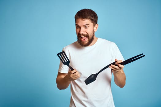 Bearded man with tools for cooking on a blue background and a white T-shirt shovel. High quality photo