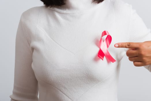 Breast cancer awareness healthcare and medicine concept. Close up Asian woman wear white shirt pointing finger to pink breast cancer awareness ribbon, studio shot isolated on white background