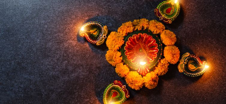 Top view overhead clay lit light a fire already on Diya or oil lamp and flower, studio shot on concrete background, Decoration of Hinduism rangoli, Happy celebration Deepavali or Diwali festival concept