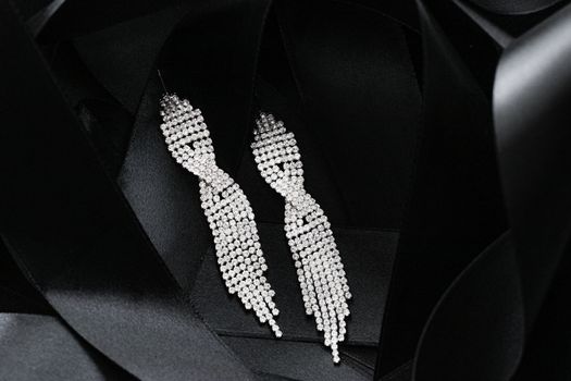 Luxury diamond earrings on black silk ribbon as background, jewelry and fashion brands