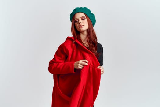 A woman holds in her hand a red coat and a dark T-shirt Green hat cropped view of a light background. High quality photo