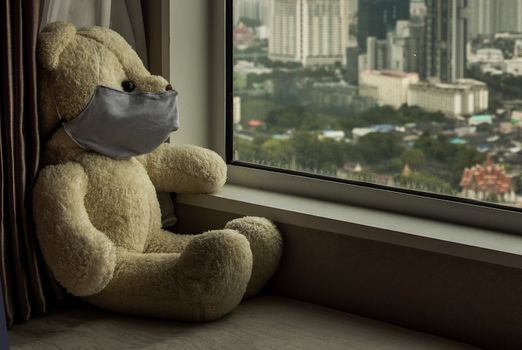 Sad teddy bear in protective medical masks sits on windowsill and looks out window. Stay at home quarantine coronavirus pandemic prevention, Virus outbreak in a world. No focus, specifically.