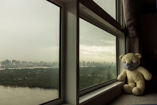 Sad teddy bear in protective medical masks sits on windowsill and looks out window. Stay at home quarantine coronavirus pandemic prevention, Virus outbreak in a world. No focus, specifically.