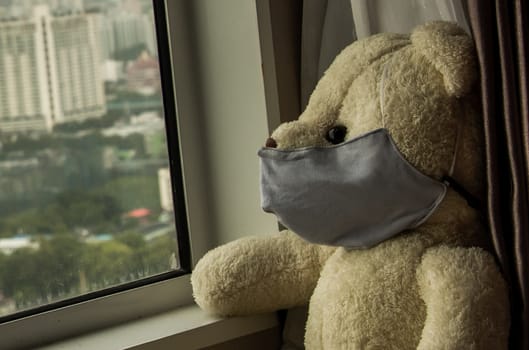 Close-up of Sad teddy bear in protective medical masks sits on windowsill and looks out window. Stay at home quarantine coronavirus pandemic prevention, Virus outbreak in a world. No focus, specifically.