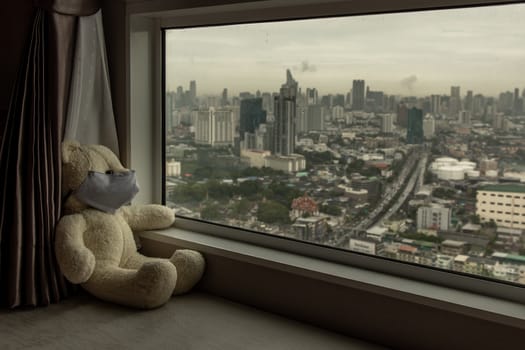 Sad teddy bear in protective medical masks sits on windowsill and looks out window. Stay at home quarantine coronavirus pandemic prevention, Virus outbreak in a world. No focus, specifically.