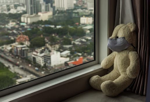 Sad teddy bear in protective medical masks sits on windowsill and looks out window. Stay at home quarantine coronavirus pandemic prevention, Virus outbreak in a world. No focus, specifically.