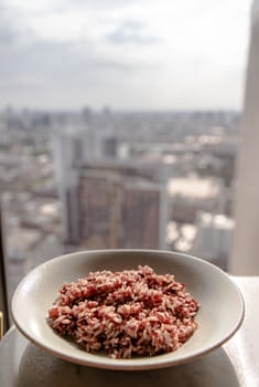 Riceberry in white dish over white table with city view at morning. Selective focus.
