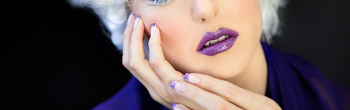 Close up of the lower face of a beautiful young woman wearing purple lipstick and nail polish