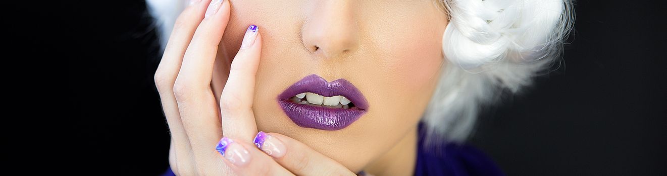 Close up of the lower face of a beautiful young woman wearing purple lipstick and nail polish