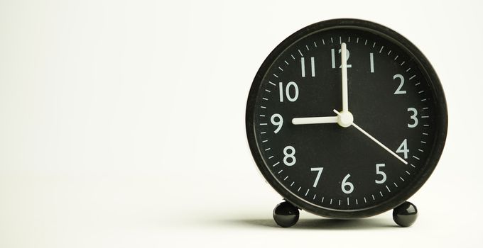 Decorative close-up black alarm clock at 9 o'clock isolated on white background with abstract copy space, start time of working day.