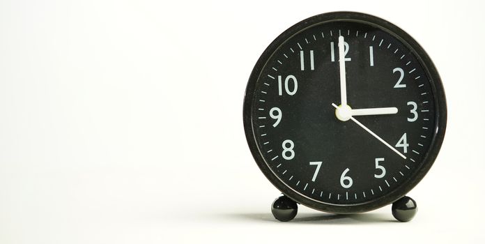 Decorative close-up black analog alarm clock for 3 o'clock or 15 o'clock, separate white background with copy space.