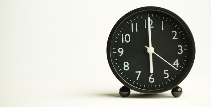 Decorative close-up black analog alarm clock for 6 o'clock or 18 o'clock, separate white background with copy space.