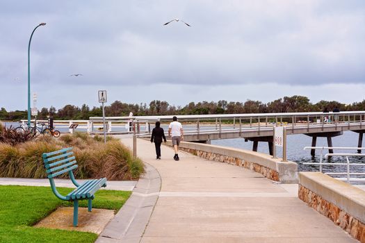 An unidentified man and woman walking along a pathway for exercise beside a lake with seagulls overhead