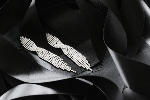 Luxury diamond earrings on black silk ribbon as background, jewelry and fashion brands