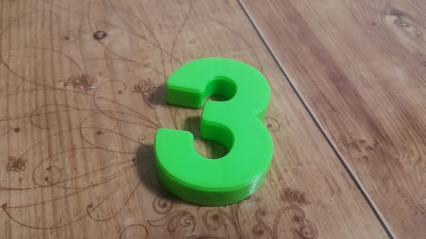 Plastic colored alphabets making words are placed on a wooden floor. These plastic letters can be used for teaching kids.