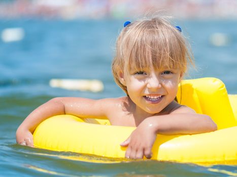 Portrait of little smiling girl with inflatable rubber circle in the sea in sunny day. Summer vacations concept.