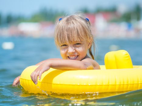 Portrait of little smiling girl with inflatable rubber circle in the sea in sunny day. Summer vacations concept.