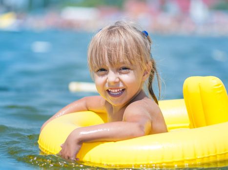 Portrait of little smiling girl with inflatable rubber circle in the sea in sunny day. Summer vacations concept.