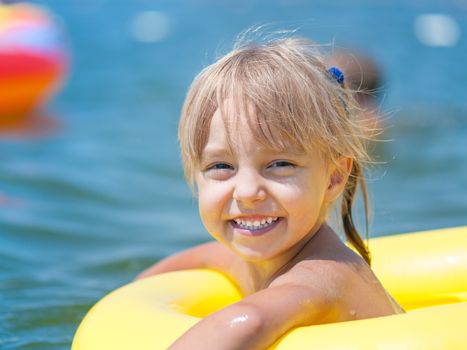 Portrait of little smiling girl with inflatable rubber circle in the sea in sunny day. Summer vacations concept.