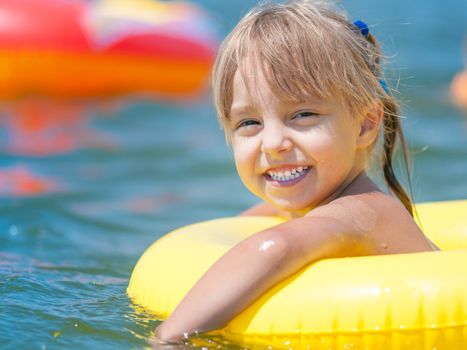 Portrait of little smiling girl with inflatable rubber circle in the sea in sunny day. Summer vacations concept.