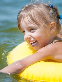 Portrait of little smiling girl with inflatable rubber circle in the sea in sunny day. Summer vacations concept.