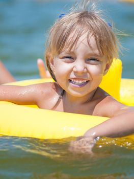 Portrait of little smiling girl with inflatable rubber circle in the sea in sunny day. Summer vacations concept.