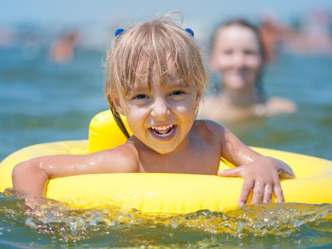 Portrait of little smiling girl with inflatable rubber circle in the sea in sunny day. Summer vacations concept.