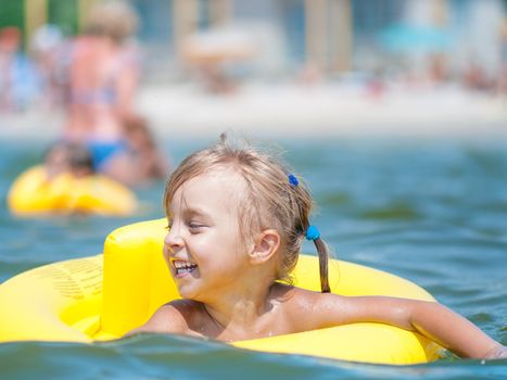 Portrait of little smiling girl with inflatable rubber circle in the sea in sunny day. Summer vacations concept.