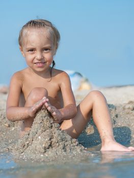 Baby girl sitting on the sandy beach and playing near the sea. Summer vacations concept.