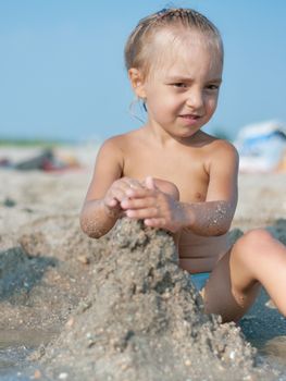 Baby girl sitting on the sandy beach and playing near the sea. Summer vacations concept.