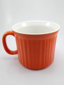 Orange heavy duty mug with handle and ridges use to pour liquid content and soup